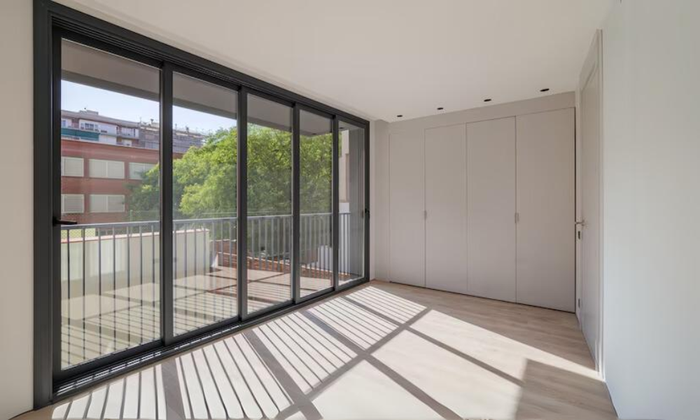 Bright room with floor-to-ceiling sliding glass doors leading to a balcony, featuring light wood floors and built-in closets, and white walls that enhance the natural light and airy feel of the space